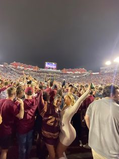 a group of people standing around each other in front of a crowd at a football game