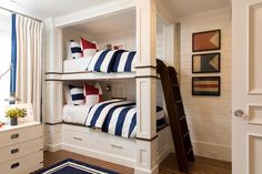 a bunk bed with blue and white striped pillows on it's bottom shelf next to a window