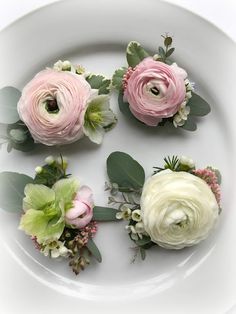 four pink and white flowers are arranged on a plate with greenery in the middle