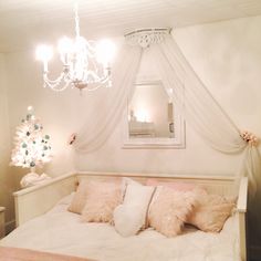 a white bed topped with lots of pillows and a chandelier hanging from the ceiling