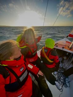 three people in life jackets on a sailboat with the sun shining through the clouds