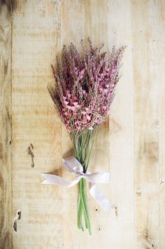 a bunch of pink flowers tied to a white ribbon on a wooden surface with wood planks in the background