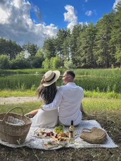 a man and woman sitting on a blanket in the grass with picnic items around them