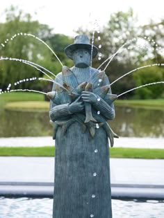 a statue with water spouting out of it's face and hands, in front of a pond