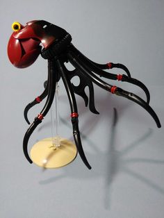 an octopus sculpture is hanging from a hook on a gray background with red and yellow accents