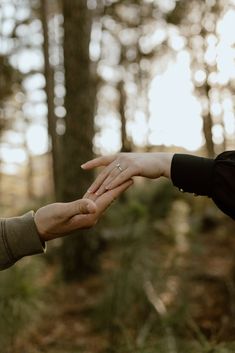 two people reaching out their hands to touch each other in the middle of a forest