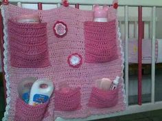 a crocheted pink blanket with baby items hanging from it's hooks in front of a crib