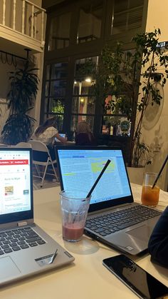 two laptops sitting on a table with drinks in front of them