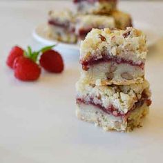 strawberry crumb bars stacked on top of each other next to a bowl of strawberries