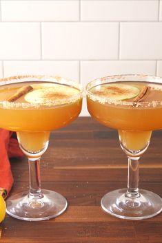 two glasses filled with drinks sitting on top of a wooden table next to an apple