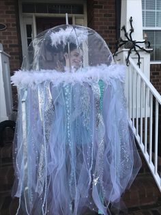 a woman wearing a costume made out of plastic and feathers, standing in front of a house