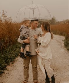 a man and woman holding an umbrella while standing next to a child on a dirt road