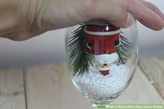 a hand holding a wine glass with a santa clause on it and pine branches in the bottom