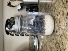 a mason jar filled with dirt sitting on top of a counter next to a faucet