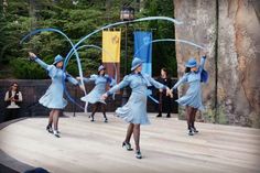 several women in blue dresses and hats are performing on stage with large hoops above their heads