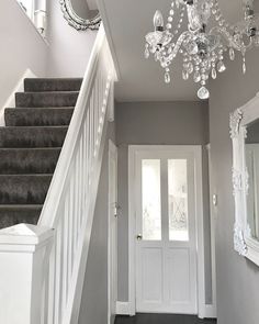 a hallway with stairs, mirror and chandelier