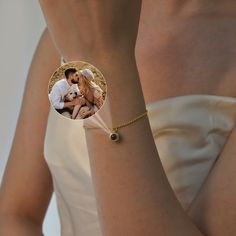 a woman wearing a white dress holding a gold bracelet with a photo on the front