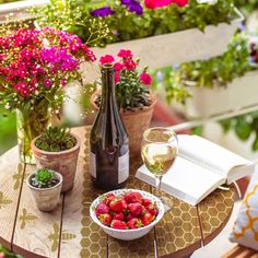 a bowl of strawberries and some wine on a table with flowers in the background