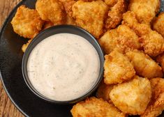 a black plate topped with tater tots next to a bowl of ranch dressing