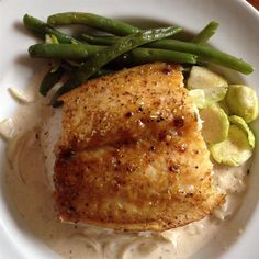 a white plate topped with meat and vegetables on top of mashed potatoes, green beans