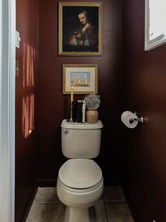 a white toilet sitting in a bathroom next to a painting on the wall above it