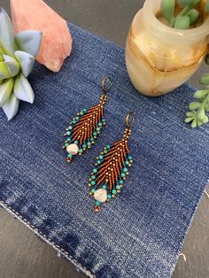 two pairs of beaded earrings sitting on top of a pair of denim jeans next to a vase with succulents