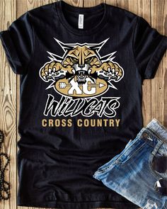 a t - shirt with the word wildcats cross country printed on it next to denim shorts