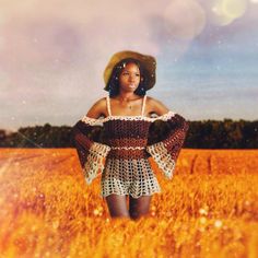 a woman standing in a field with her hands on her hips wearing a straw hat