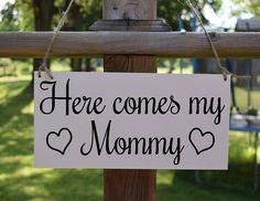 a sign that says here comes my mommy hanging on a fence in front of some grass