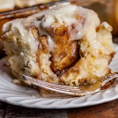 a piece of cinnamon roll with icing on a white plate next to a fork