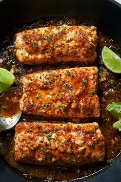 three salmon fillets in a skillet with sauce and limes on the side