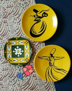 two yellow plates with designs on them are sitting next to each other and one has a flower in front of it