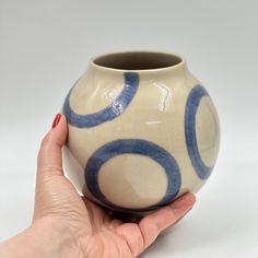 a hand holding a blue and white vase with circles painted on the outside of it