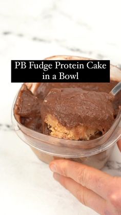 a hand holding a plastic container filled with chocolate cake in it's bottom and the text pb fudge protein cake in a bowl