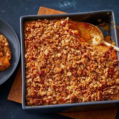 a pan filled with food next to two plates on a wooden cutting board and spoon