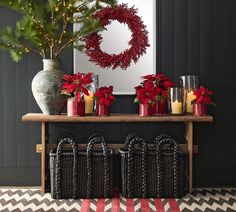 a table with baskets and candles on it in front of a christmas wreath, surrounded by poinsettis