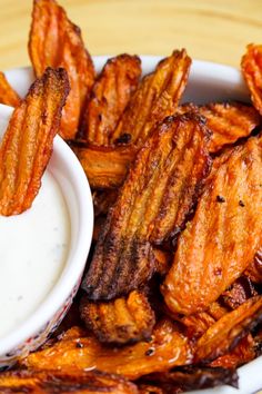 some fried food is in a white bowl on a wooden table with a dipping sauce