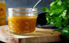 a glass jar filled with mustard sitting on top of a wooden cutting board next to green peppers