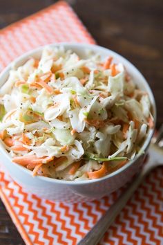 a white bowl filled with coleslaw on top of an orange and white napkin