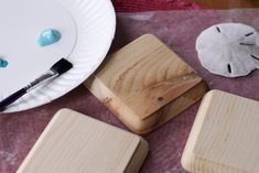 three wooden coasters sitting on top of a table next to a paper plate and paintbrush