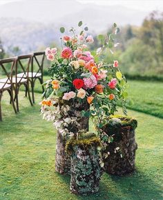 three wooden stumps with flowers in them sitting on the grass next to a bench