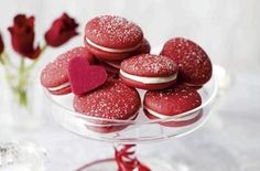 red velvet macaroons in a glass dish on a white tablecloth with flowers