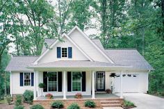 a white house with black shutters in the front yard and landscaping around it, surrounded by trees