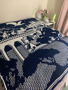 a blue and white blanket on top of a bed next to a vase with flowers