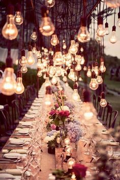 a long table with lots of lights hanging from it's ceiling and flowers in the center