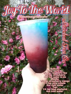 a hand holding up a blue and red drink in front of pink flowers with the words joy to the world on it