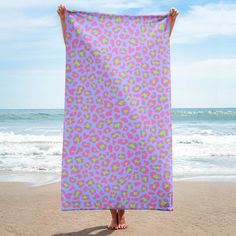 a person standing on the beach holding up a pink and green flowered towel over their head