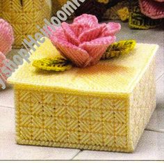 a crocheted box with a pink flower on top and two other knitted items in the background