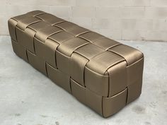 a gold leather bench sitting in front of a white brick wall on concrete flooring