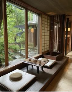 a room that has some tables and chairs on it in front of large windows with trees outside